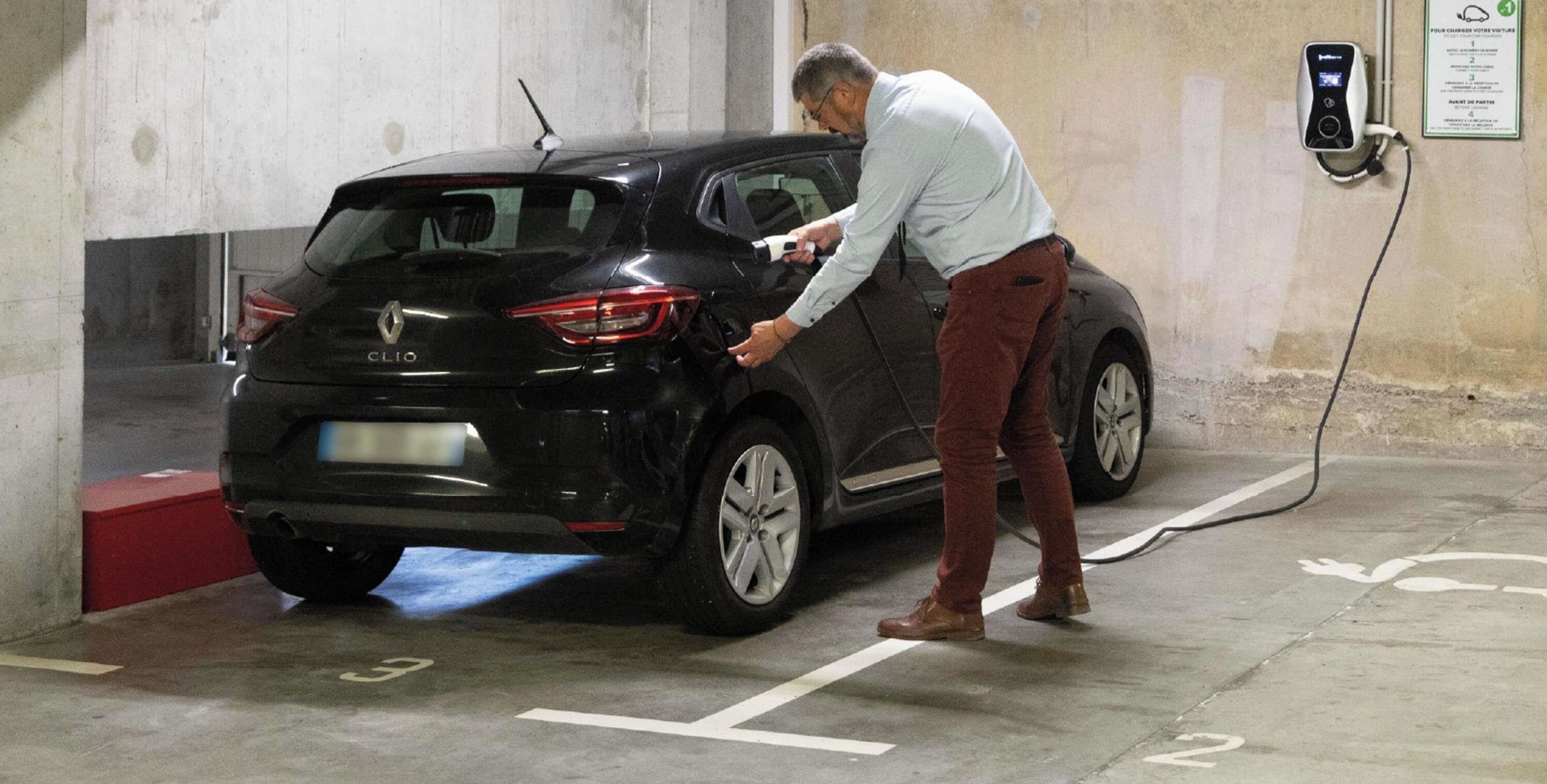 Iemand laadt een zwarte Renault Clio op in een parkeergarage.