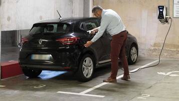Iemand laadt een zwarte Renault Clio op in een parkeergarage.