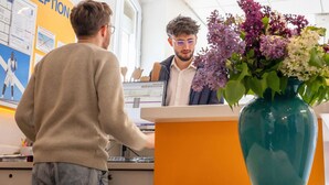 Un área de recepción con un mostrador, una computadora y un florero con flores.