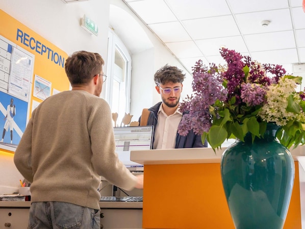 Un área de recepción con un mostrador, una computadora y un florero con flores.