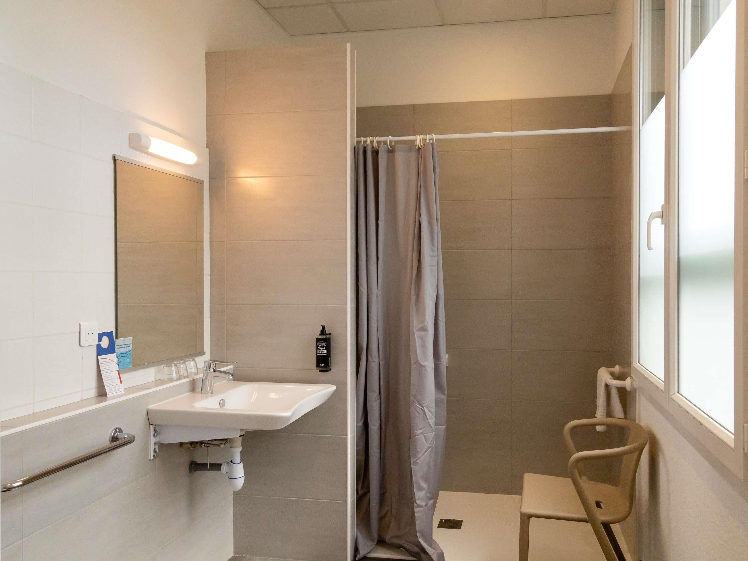 Ein Badezimmer mit Dusche, Waschbecken, einem Stuhl und einem Fenster.