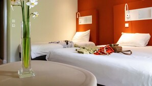 Habitación de hotel con dos camas, un florero con flores y una mesa con un bolso.