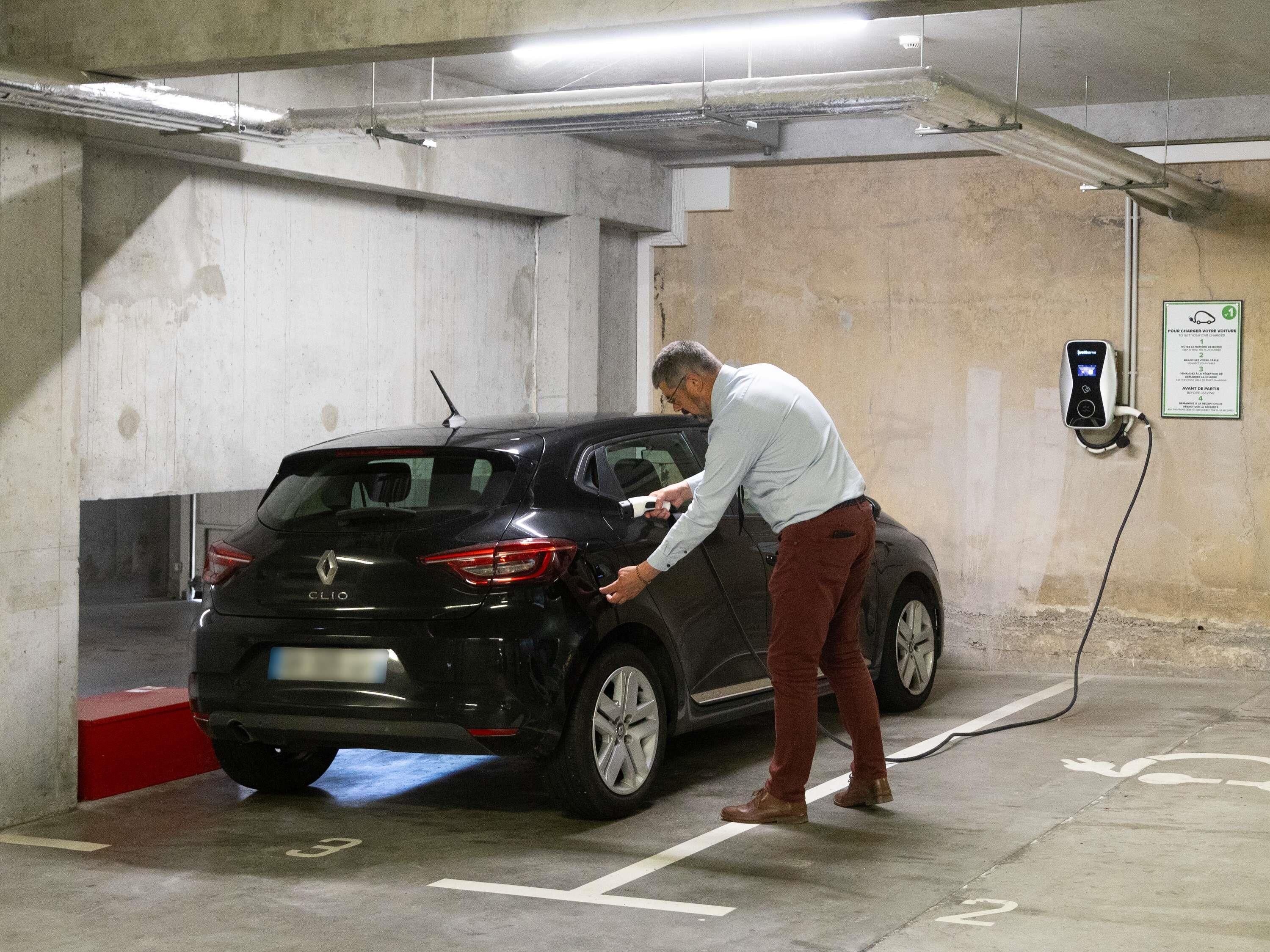 Un aparcamiento con estación de carga para coches, paredes de hormigón y un cartel con indicaciones.