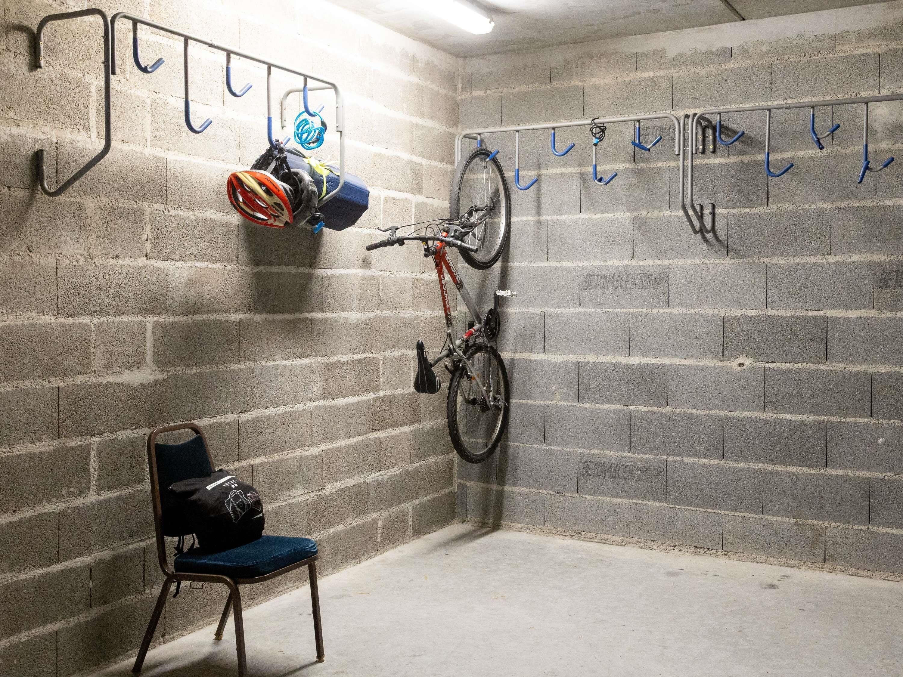 Una habitación con pared de bloques de concreto, una bicicleta montada en un soporte, una silla con un bolso y un soporte para bicicletas con ganchos.