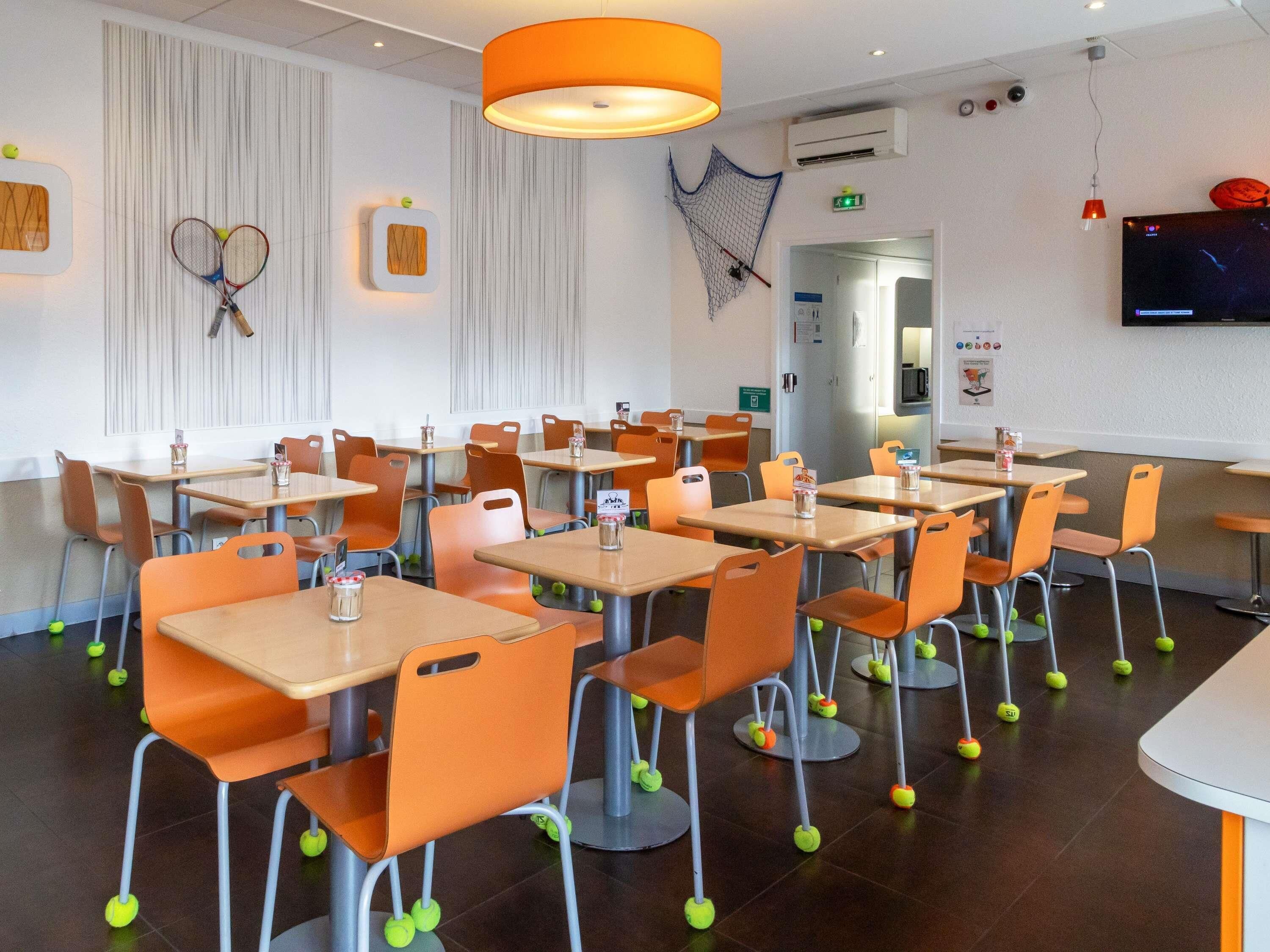 A dining area with tables and chairs, tennis rackets on the wall, and a TV screen.