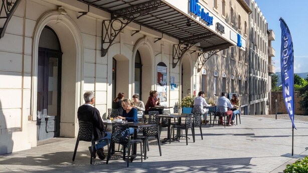 Un café al aire libre con mesas y sillas, un edificio con un letrero que dice 