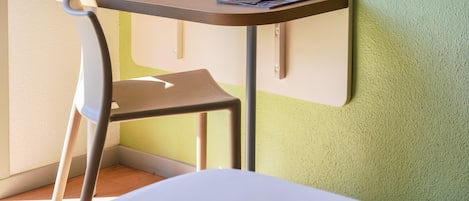 Un pequeño escritorio en esquina con una silla, una revista y un control remoto encima.