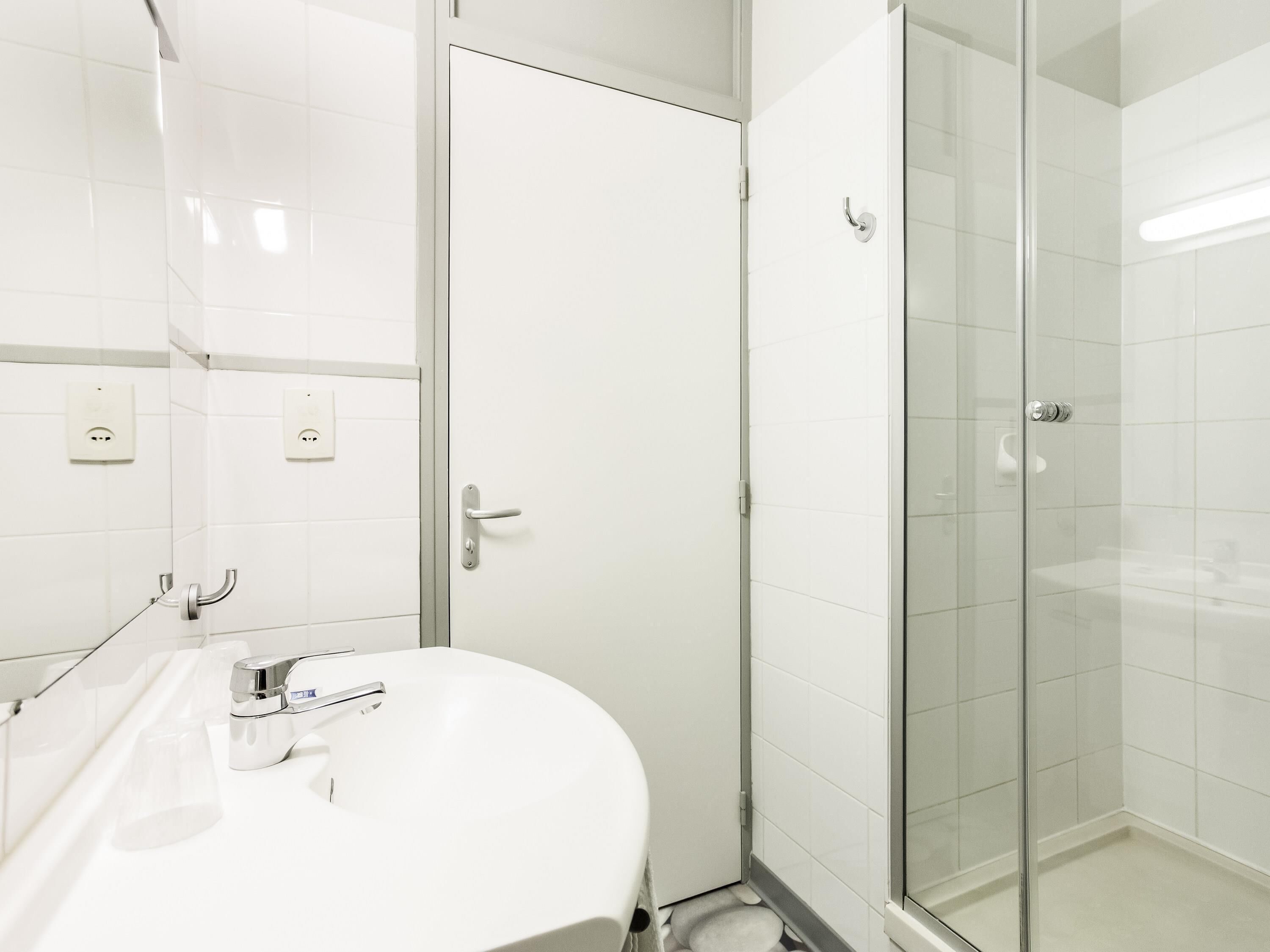 Une salle de bain moderne avec un lavabo blanc, une douche en verre et une porte dotée d’une poignée argentée.