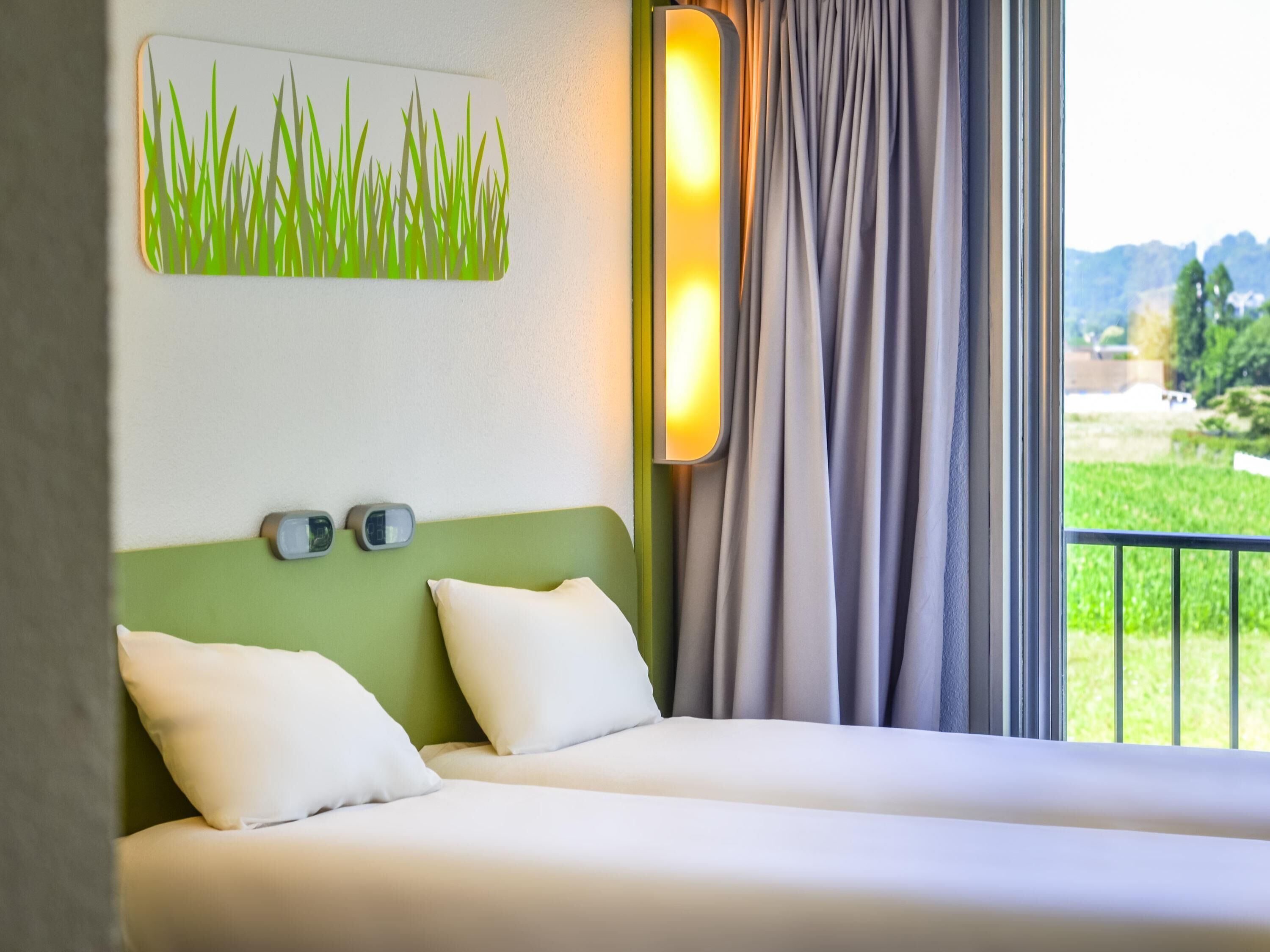 Ein Hotelzimmer mit zwei Betten, einem grünen Kopfteil, einer Wanduhr und Blick auf Grünfläche.
