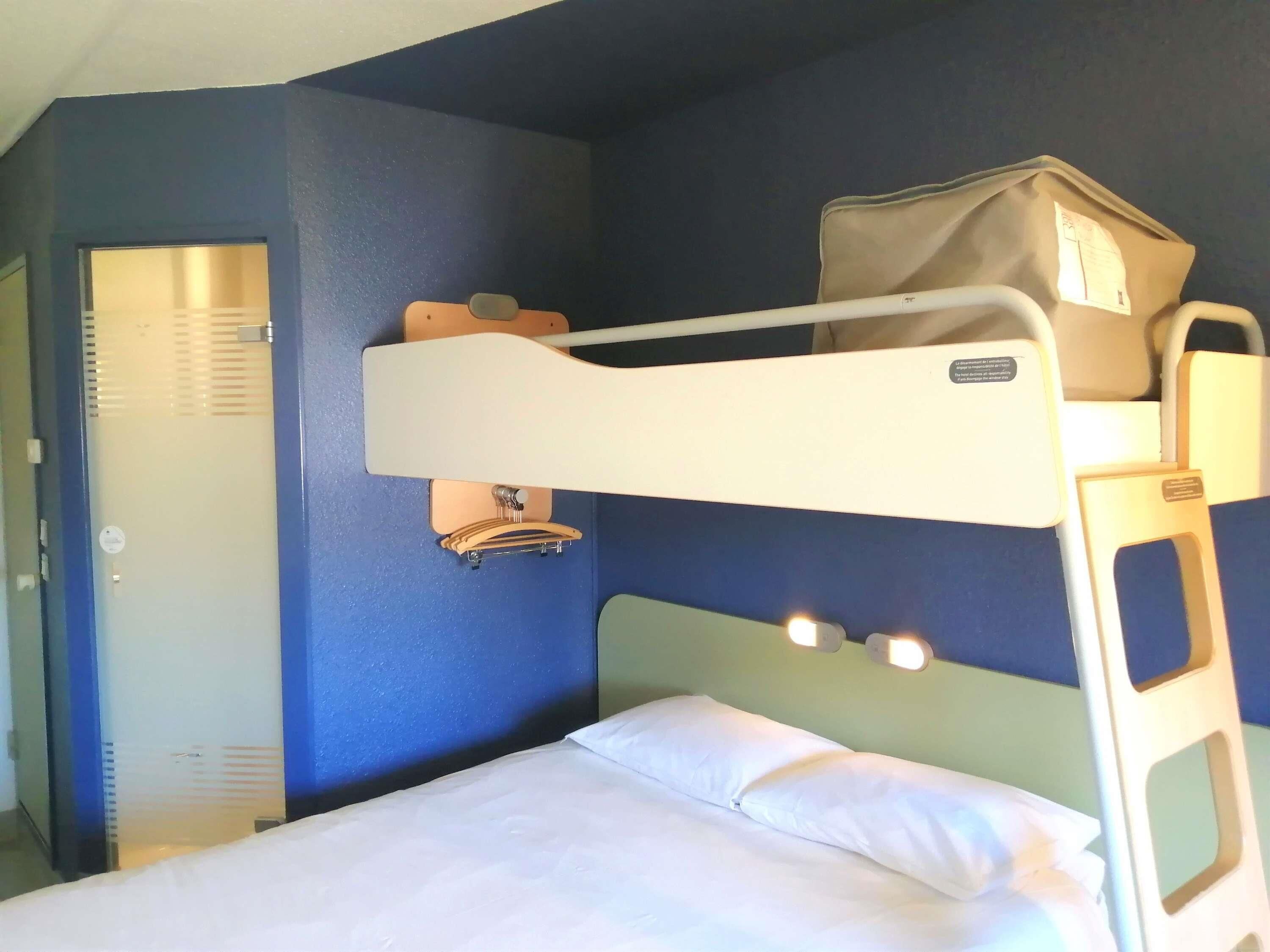 A bunk bed with a suitcase on top, a bedside table with a lamp, and a door with a handle.