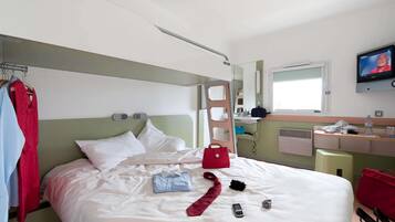 Une chambre d’hôtel avec un lit, une télévision, un bureau avec un miroir et une fenêtre.