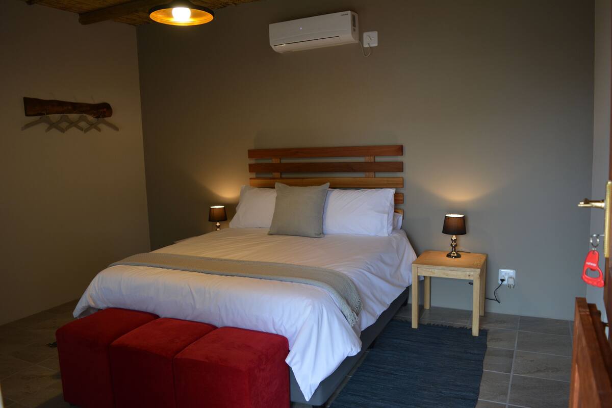 Une chambre à coucher avec un lit, des lampes de chevet, un banc rouge et un appareil de climatisation.