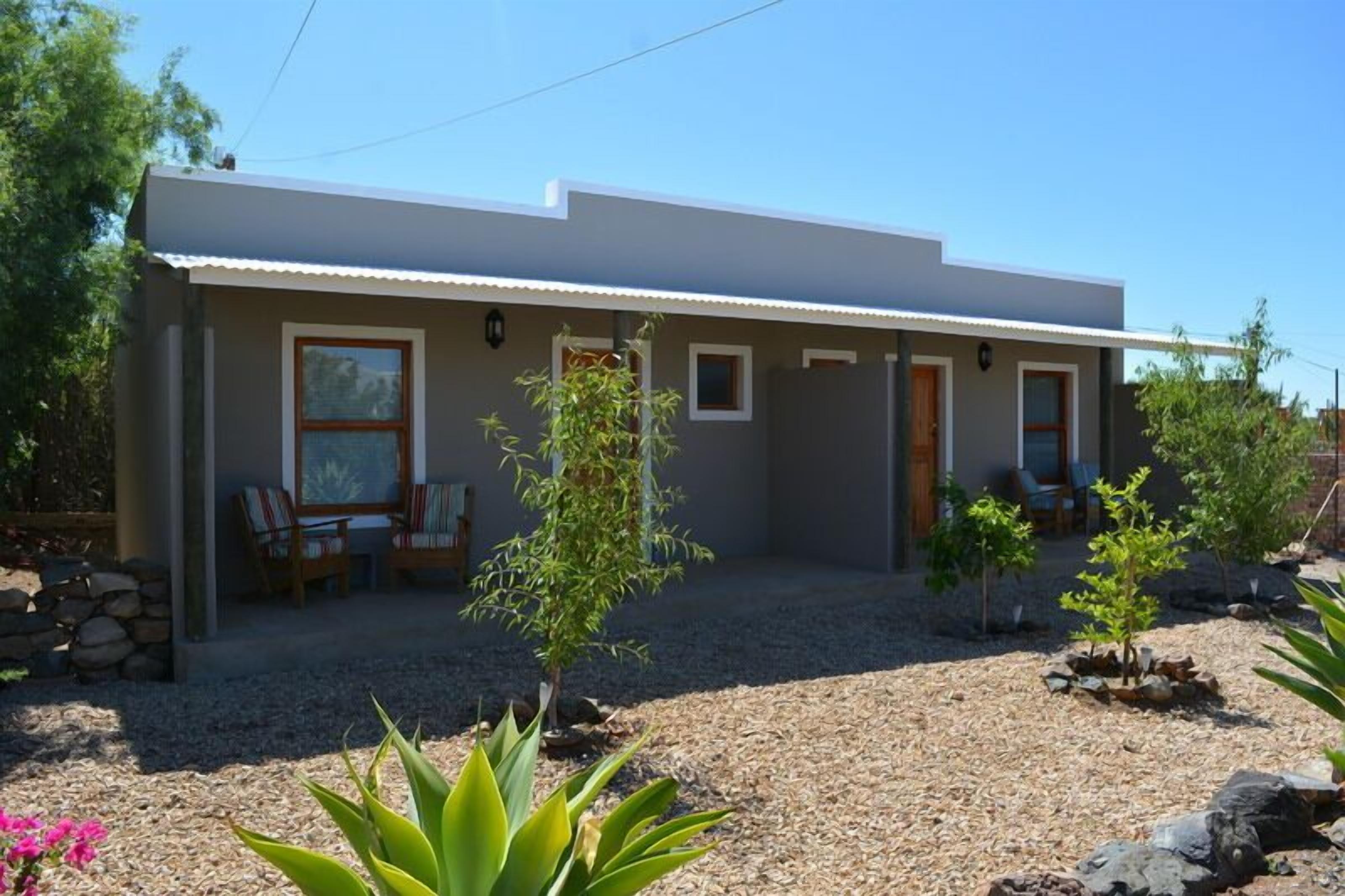 A modern single-story house with a covered patio, a small garden with various plants, and a gravel driveway.