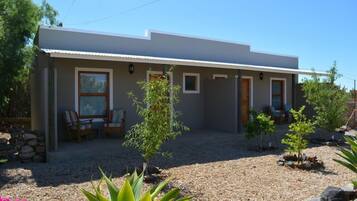 A modern single-story house with a covered patio, a small garden with various plants, and a gravel driveway.