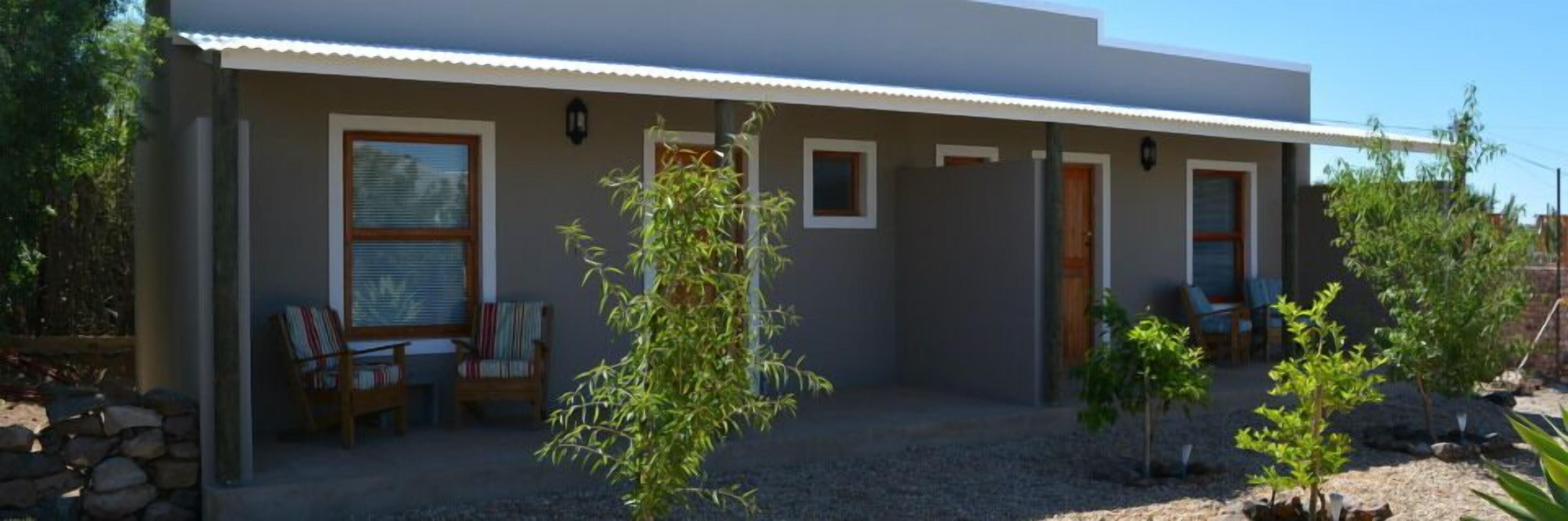 A modern house with a covered patio, a small garden, and a seating area with chairs.