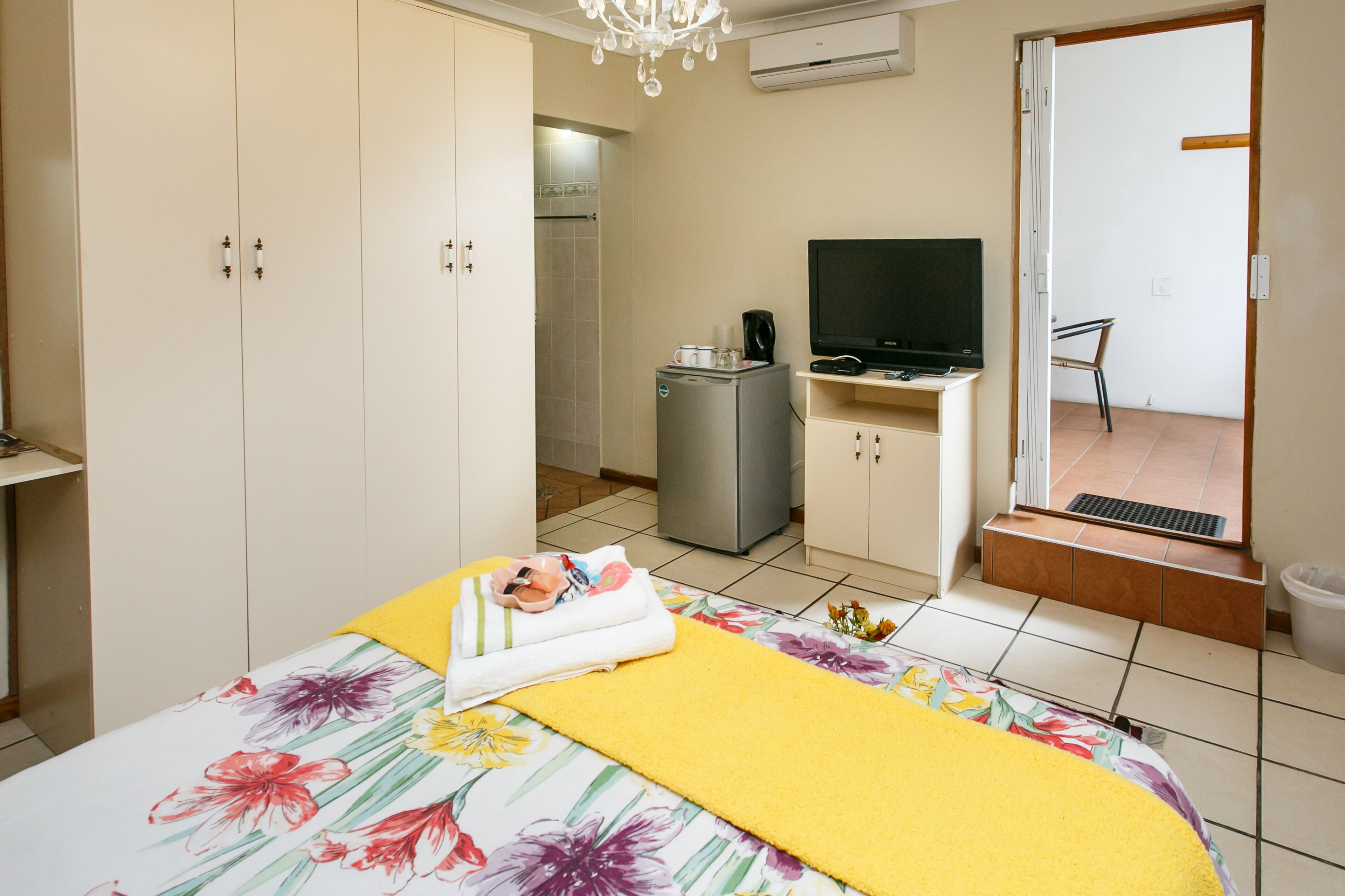 Un dormitorio con cama, televisión, refrigerador y un baño visible a través de una puerta abierta.