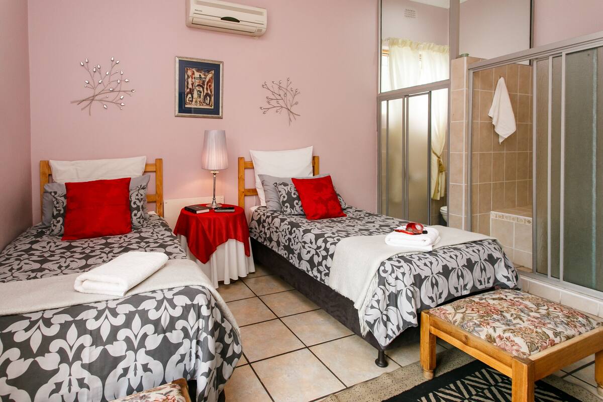Une chambre avec deux lits, une petite table, un banc et un espace douche.