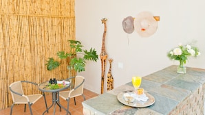 Un coin repas comprenant une table, des chaises, une sculpture de girafe, des chapeaux accrochés au mur et un vase rempli de fleurs.