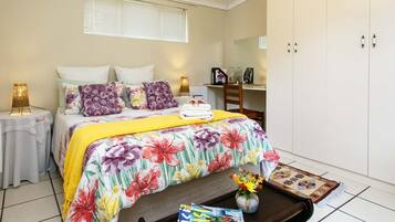 Quarto com cama, mesas de cabeceira, escrivaninha, guarda-roupa e janela com persianas.