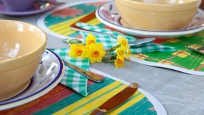 Une table à manger avec des bols et des couverts, un chemin de table à carreaux et des fleurs jaunes.