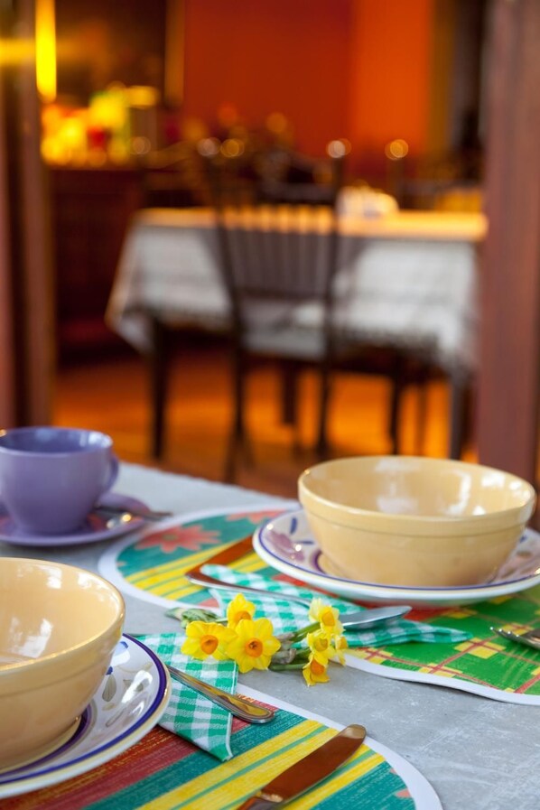 A dining table with a colorful tablecloth, a set of bowls, a spoon, and a bouquet of yellow flowers.