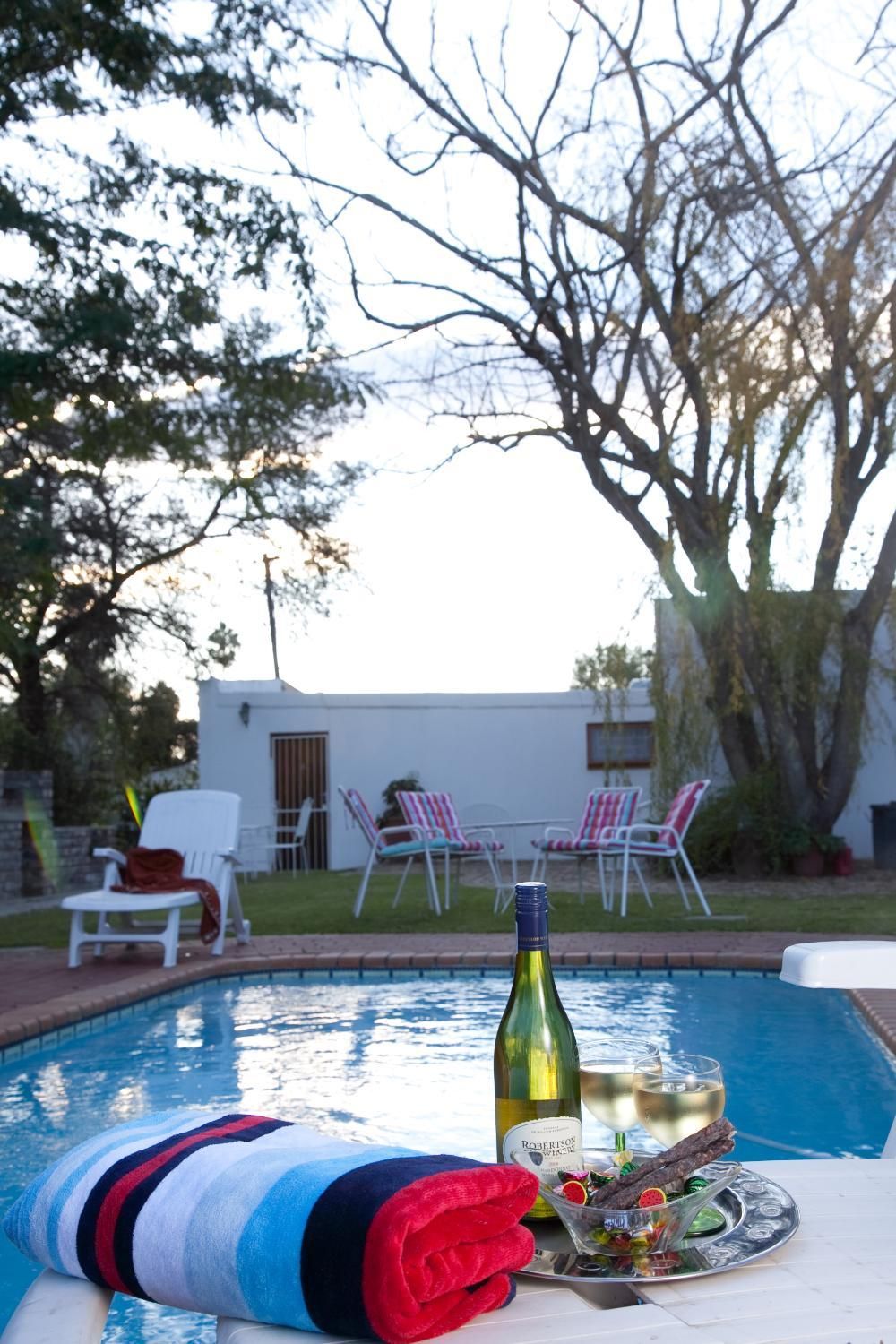 Escena junto a la piscina con una botella de vino, copas y una bandeja con aperitivos.