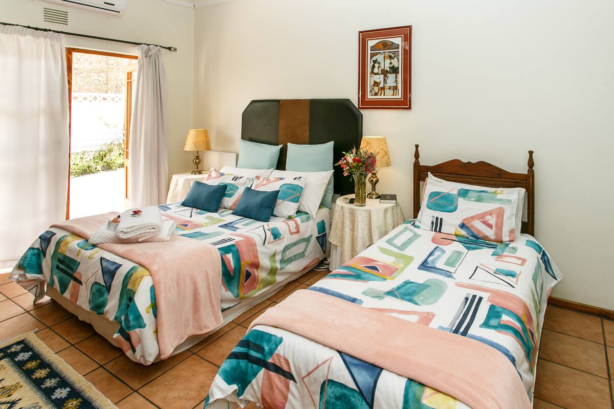 Un lit double avec une couvre-lit aux motifs géométriques colorés, une table de chevet avec une lampe et un tableau encadré au mur.