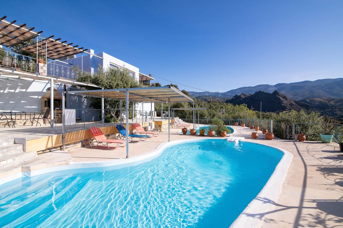 A swimming pool with a pergola, lounge chairs, and potted plants.