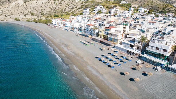 An aerial view of a coastal town with a beach, buildings, and clear blue waters. - Sarakinas Residences (Ierapetra)