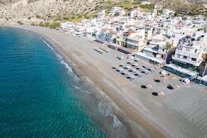 An aerial view of a coastal town with a beach, buildings, and clear blue waters. - Sarakinas Residences (Ierapetra)