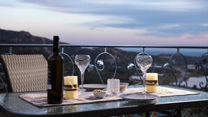 A table set with a bottle, glasses, candles, and a bowl on a balcony overlooking a scenic view. - Sarakinas Residences (Ierapetra)