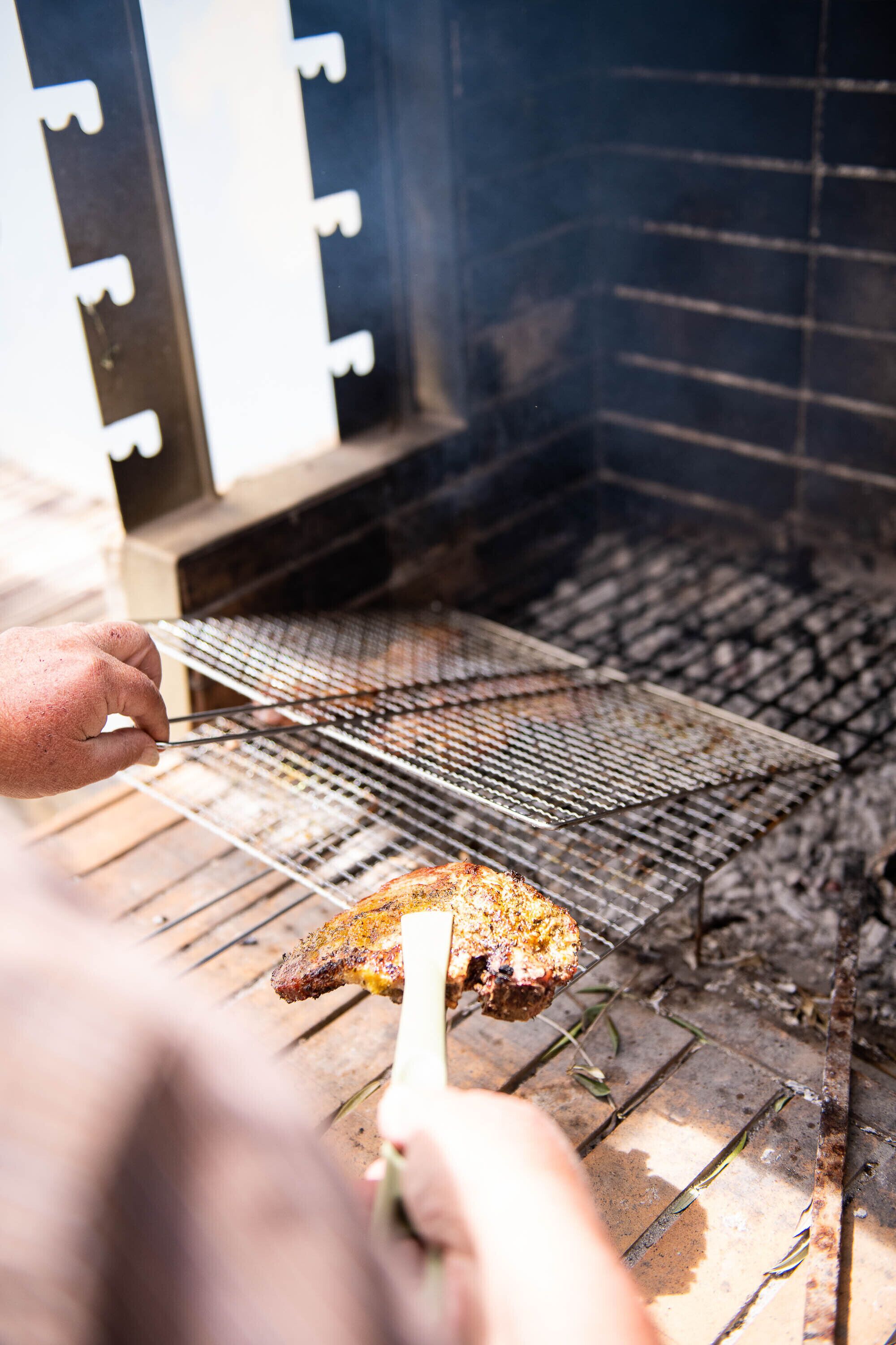 Una persona asando carne en una parrilla al aire libre.