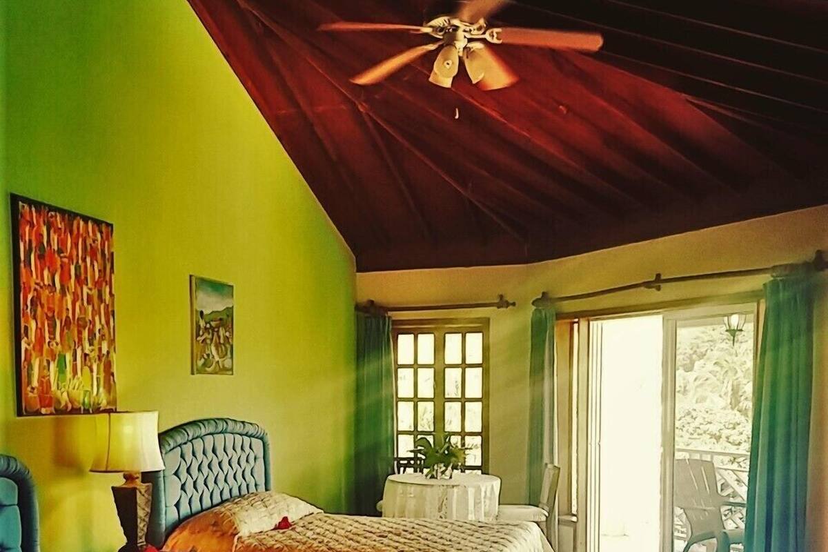 Ein Schlafzimmer mit zwei Betten, einem Deckenventilator, einem Fenster mit Vorhängen und Blick ins Freie.
