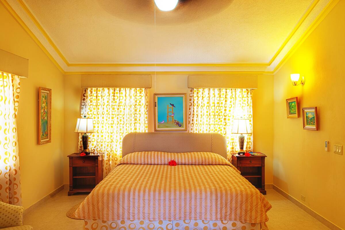 Ein Hotelzimmer mit einem großen Bett, zwei Nachttischen, einem Wandbild und Vorhängen mit einem Rundmuster.
