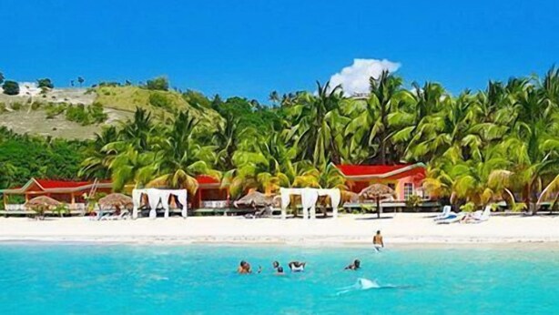 A beach resort with clear turquoise waters, palm trees, and red-roofed buildings. - Abaka Bay Resort (Ile-a-Vache)