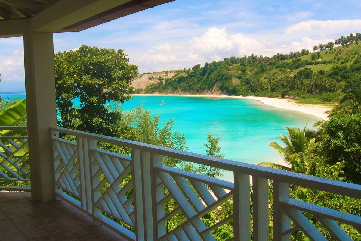 Ein Balkon mit Blick auf einen türkisblauen Strand und üppiges Grün.