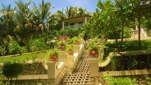 A staircase leading to a house with a balcony, surrounded by lush greenery and potted plants. - Abaka Bay Resort (Ile-a-Vache)