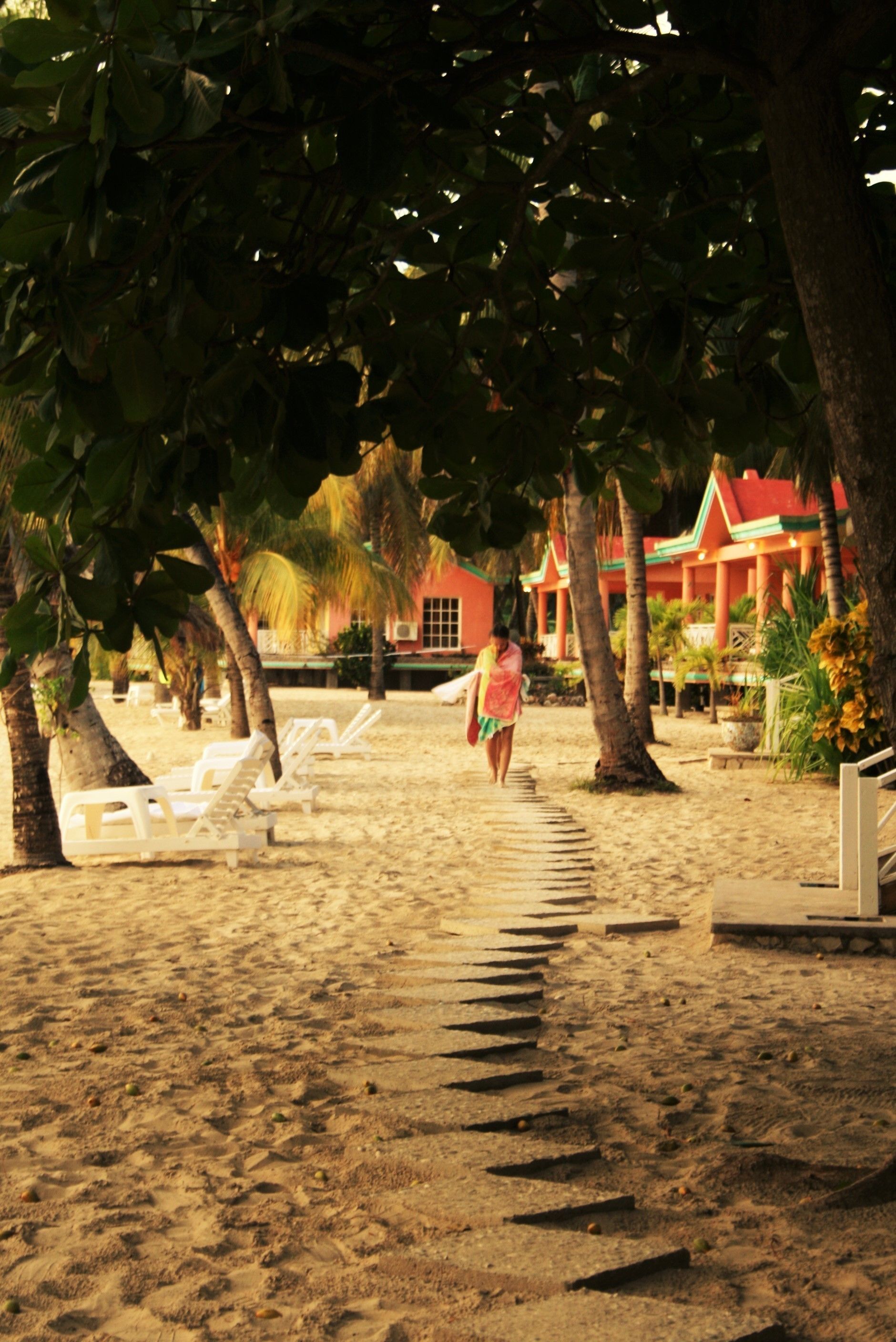 A beach with lounge chairs and a pathway leading to a building with a red roof.