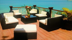 A terrace with outdoor furniture, a view of the sea, and a wooden deck railing. - Abaka Bay Resort (Ile-a-Vache)