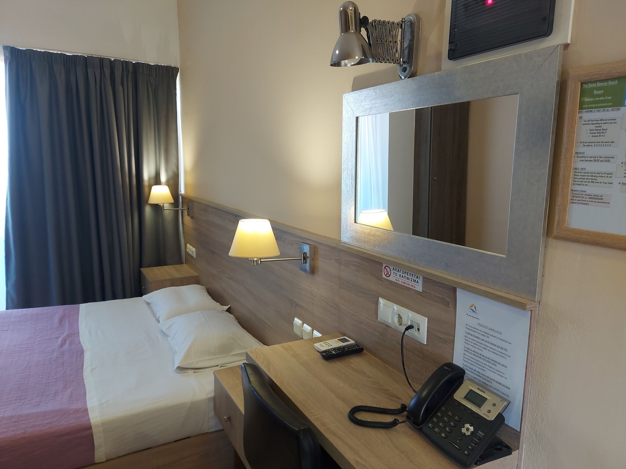 A hotel room with a bed, bedside table, lamp, phone, and a mirror.