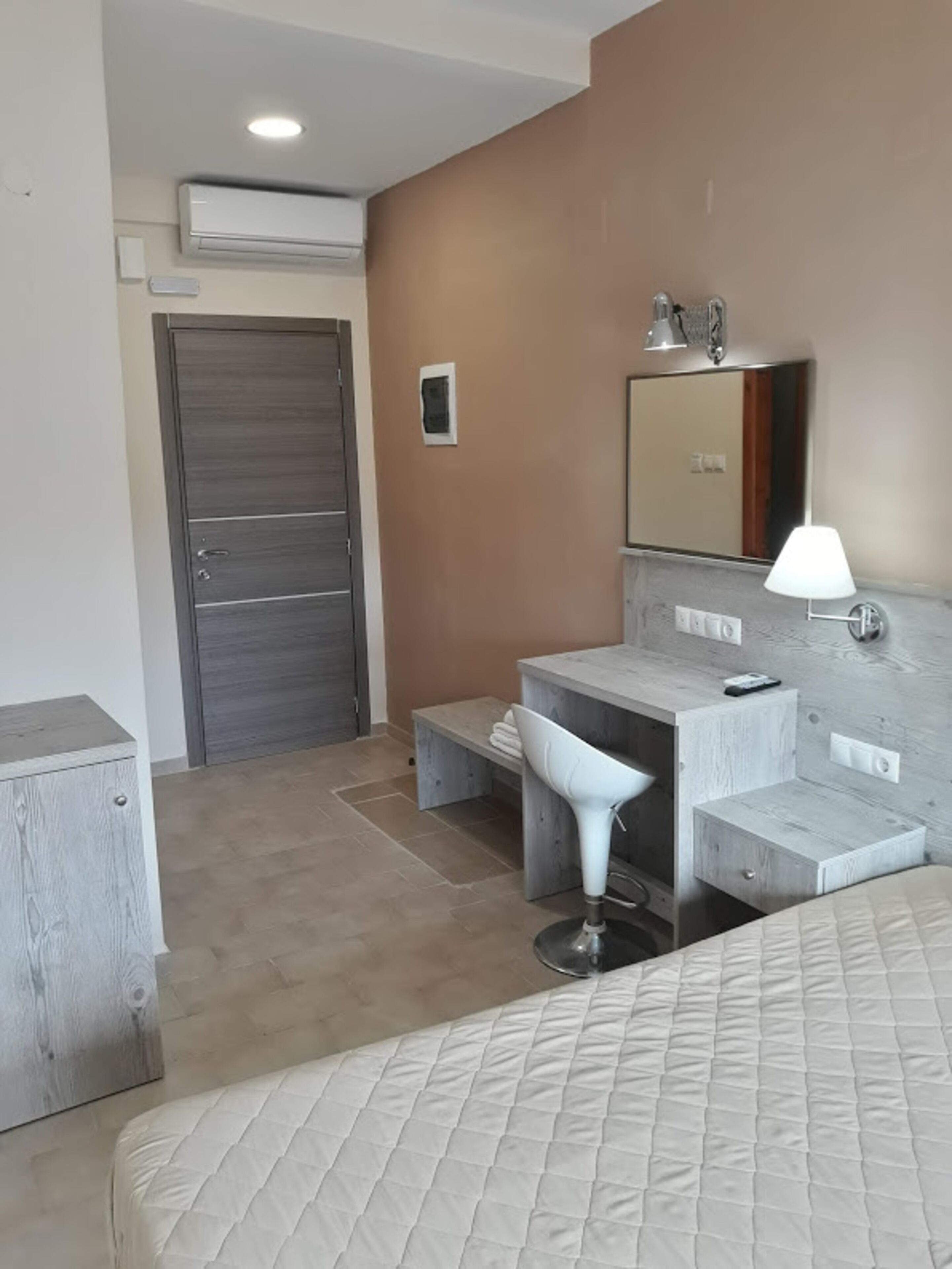 Een hotelkamer met een bed, een bureau met stoel, een kaptafel met spiegel en een deur.