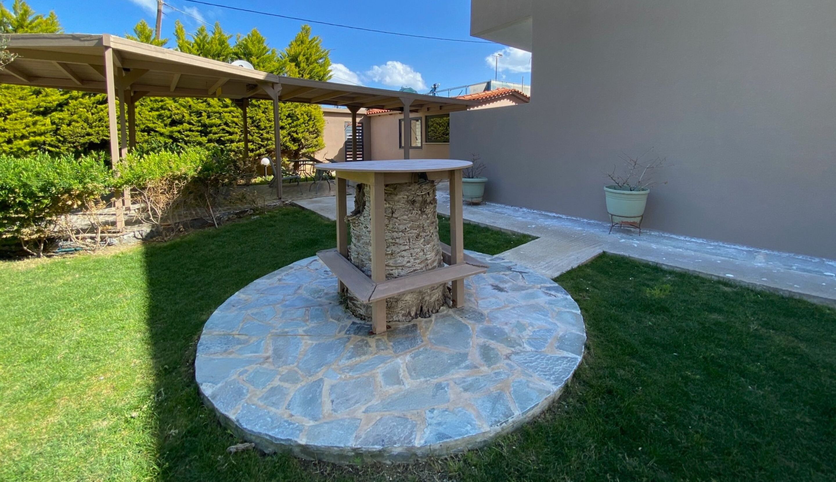 A stone-tiled patio with a wooden table and a pergola structure.