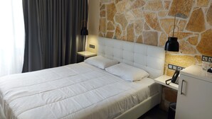 Habitación de hotel con una cama grande, una pared decorativa de piedra, una mesita de noche con lámpara y un armario pequeño.