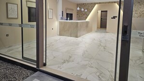 Un hall de hotel con mostrador de recepción, suelo de mármol y un separador de vidrio.