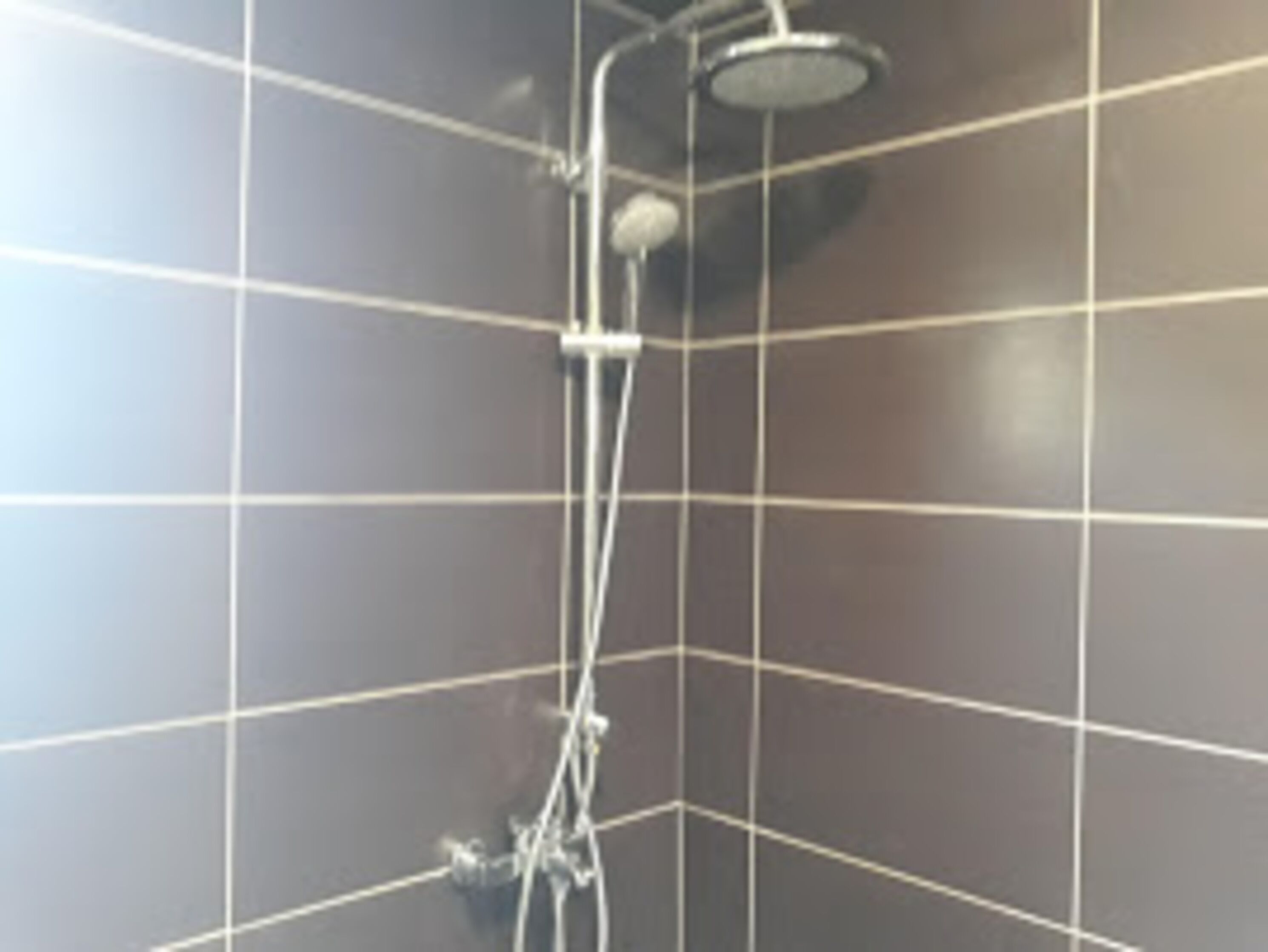 A tiled shower area with a handheld showerhead and a wall-mounted faucet.