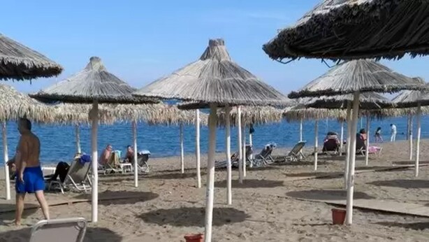 Una playa con sombrillas de paja y sillas de descanso.