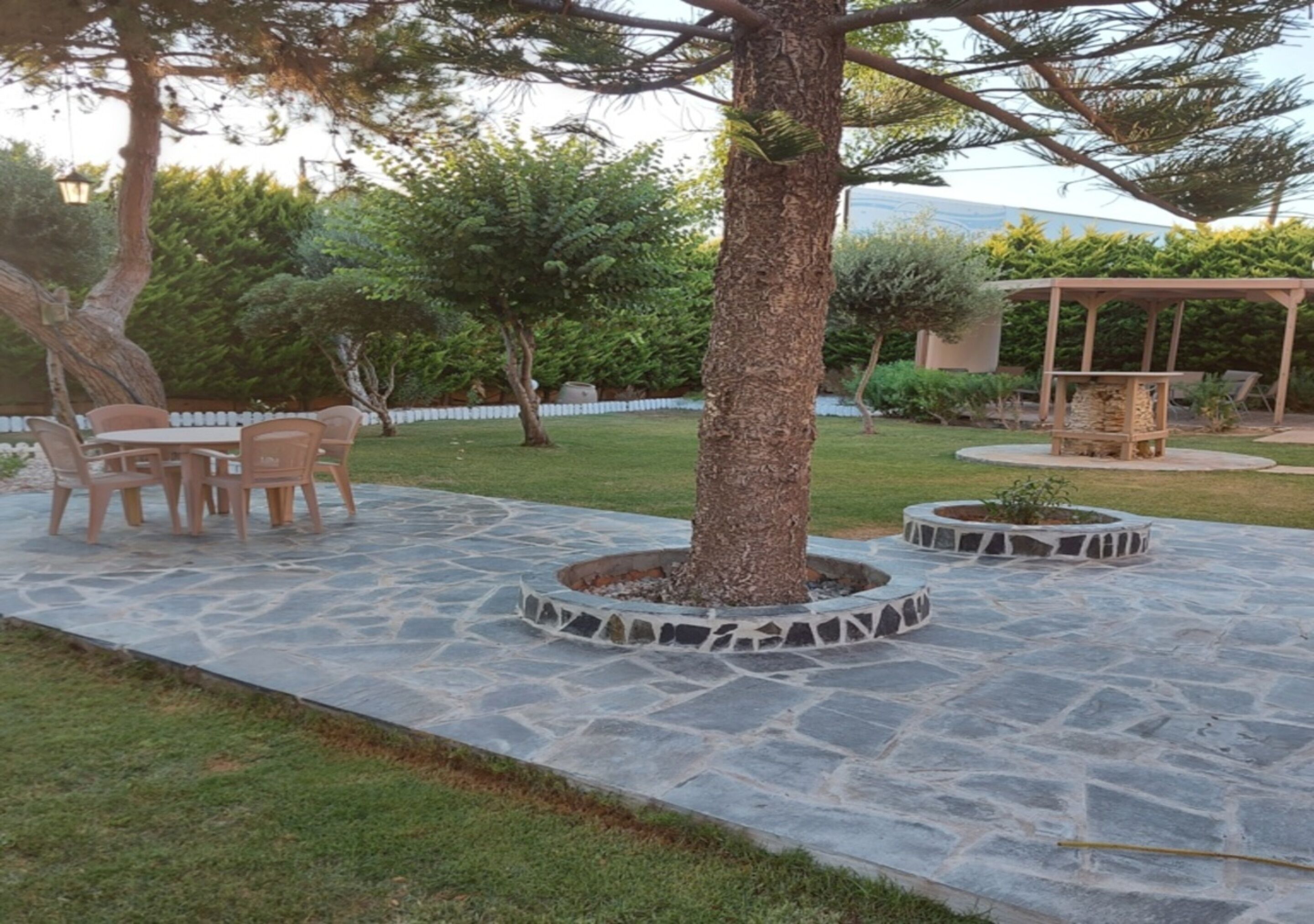 Un patio con suelo de piedra, una mesa de madera con sillas y un árbol en el centro.