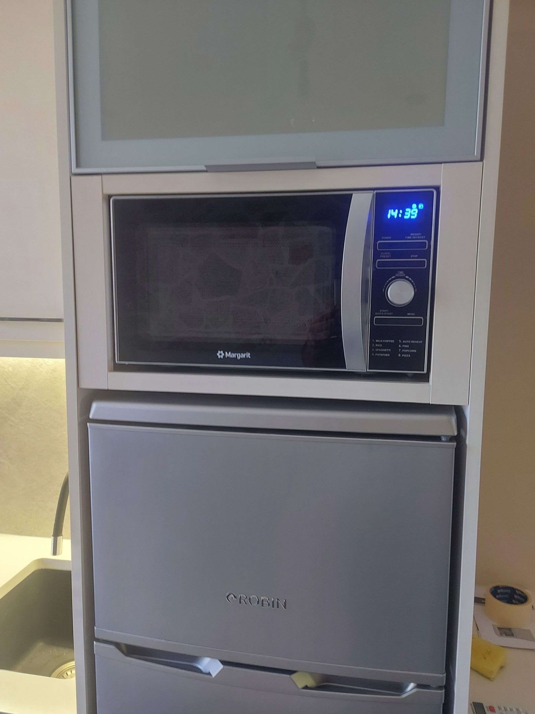 Eine Küche mit Mikrowelle, Backofen und einer digitalen Uhr, die 14:39 Uhr anzeigt.
