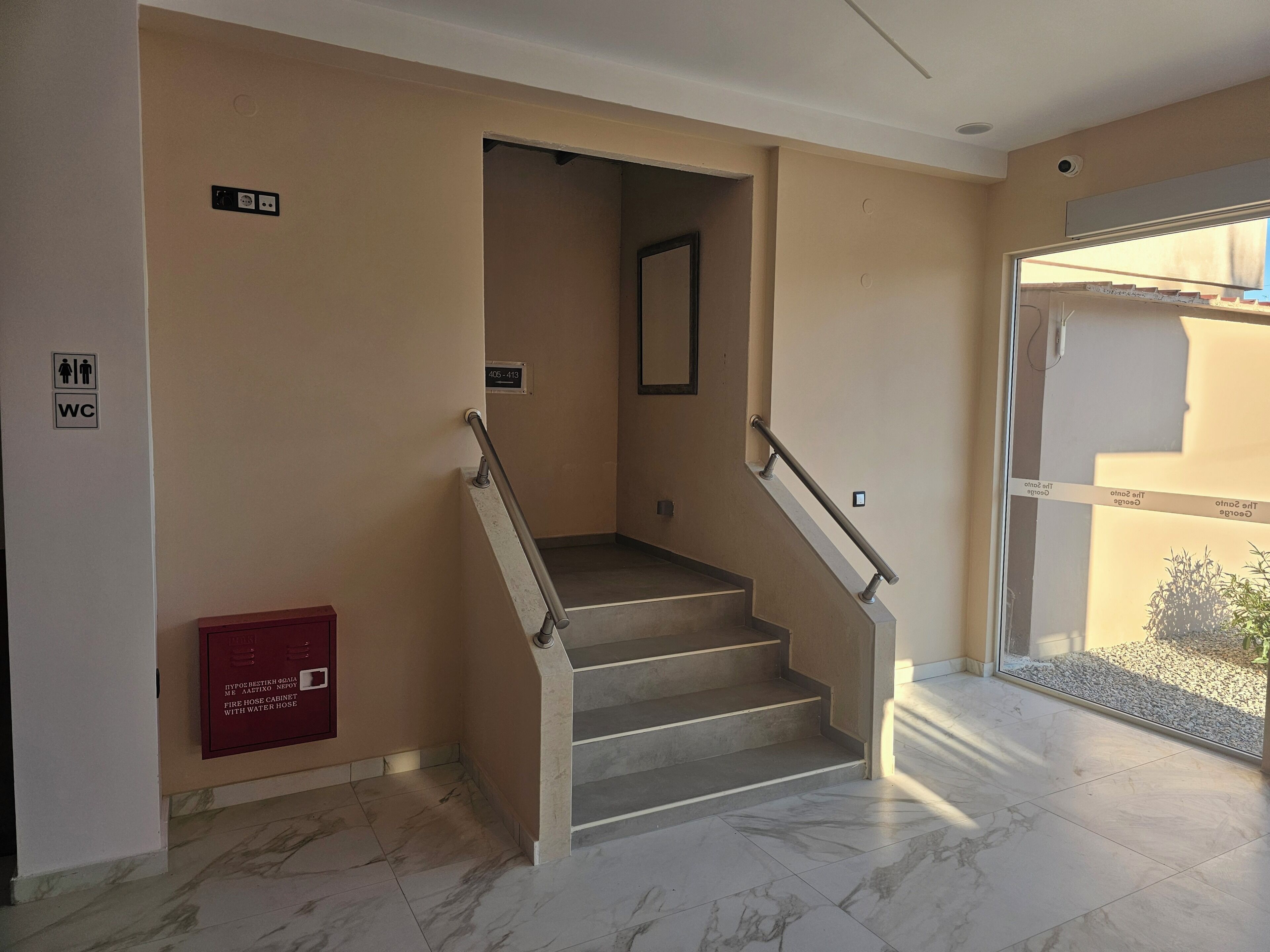 A staircase with a fire hose cabinet, a WC sign, and a door leading to an outdoor area.
