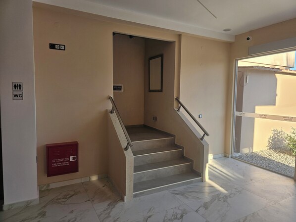 A staircase with a fire hose cabinet, a WC sign, and a door leading to an outdoor area. - The Santo George Beach Resort (Malevizi)